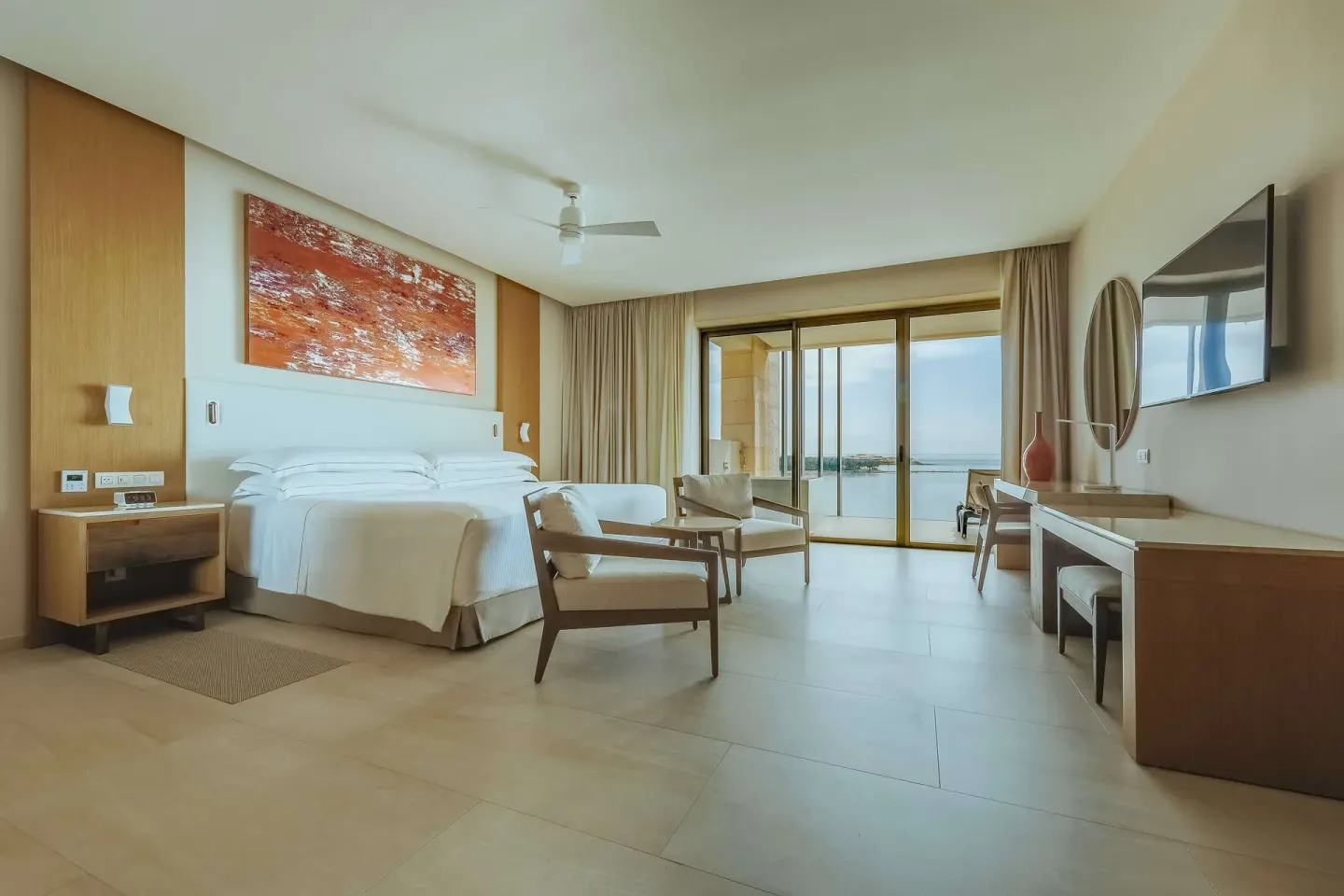 Guest room with king bed, armchairs, desk, and sea-facing balcony at Barceló Maya Riviera.