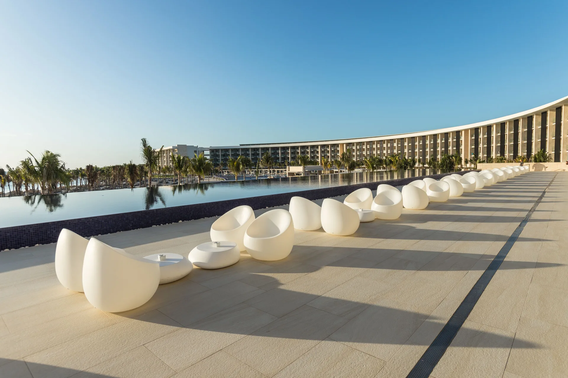 Pool terrace with white lounge chairs and resort building at Barceló Maya Riviera.