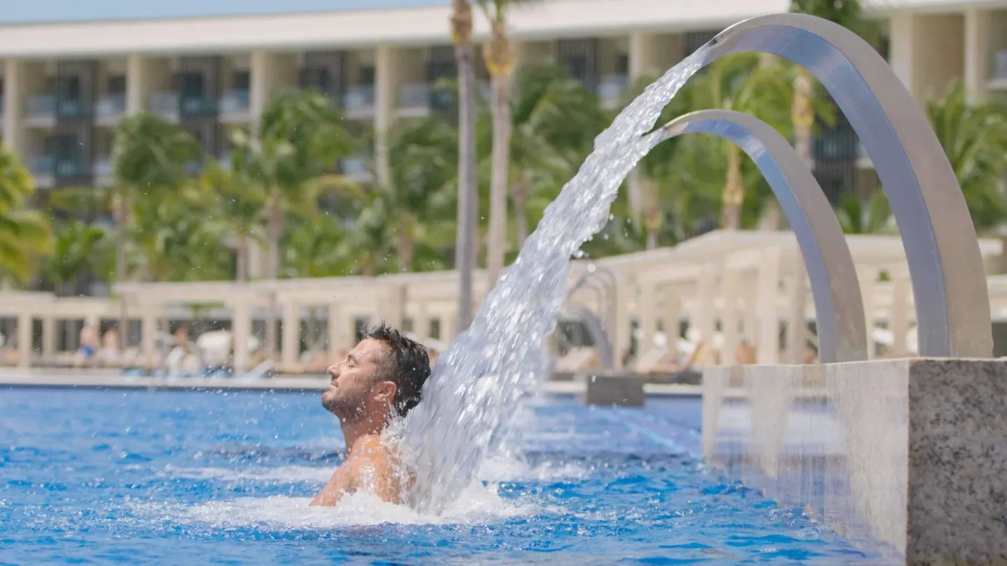 Guest under an arched pool water feature at Barceló Maya Riviera.