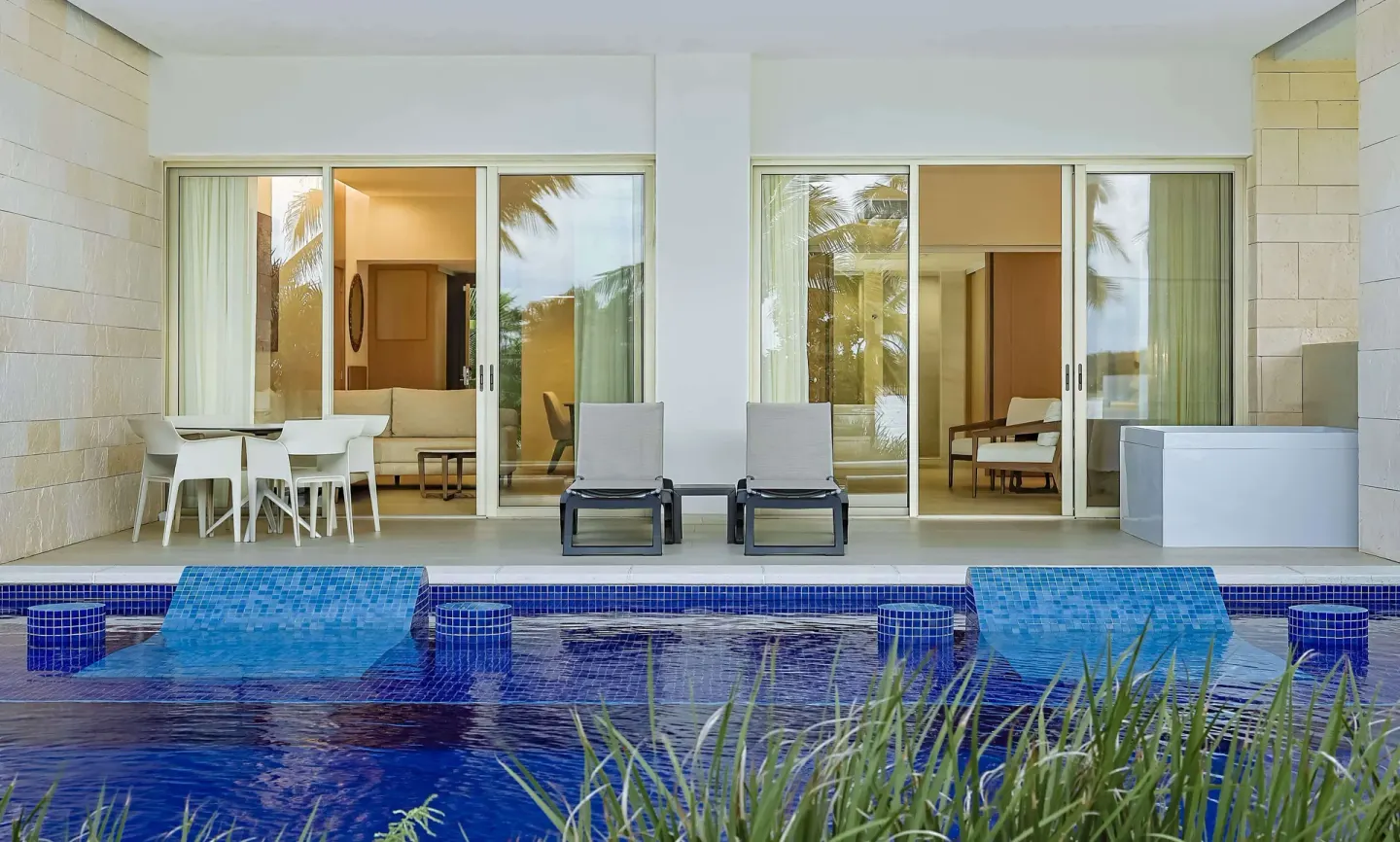Swim-up patio with sliding doors, loungers, and blue pool at Barceló Maya Riviera.