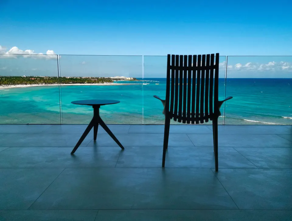 Junior Suite Oceanfront balcony with chair, table, and turquoise sea at Barceló Maya Riviera.