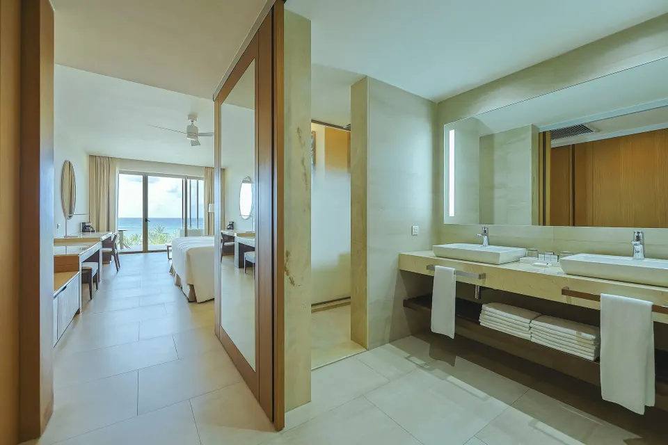 Junior Suite Oceanfront bathroom with twin sinks and bedroom beyond at Barceló Maya Riviera.