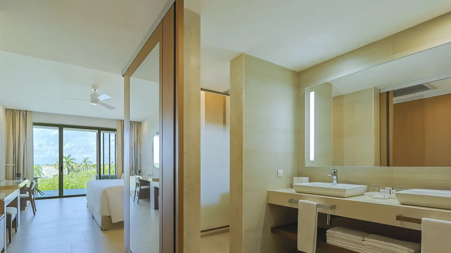 Junior Suite bathroom with double sinks and bedroom view at Barceló Maya Riviera.