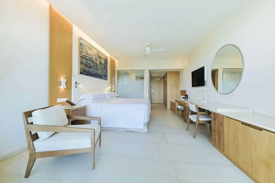 Junior Suite with king bed, armchair, desk and round mirror at Barceló Maya Riviera.