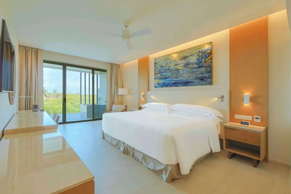 Junior Suite king bed with balcony doors and greenery outside at Barceló Maya Riviera.