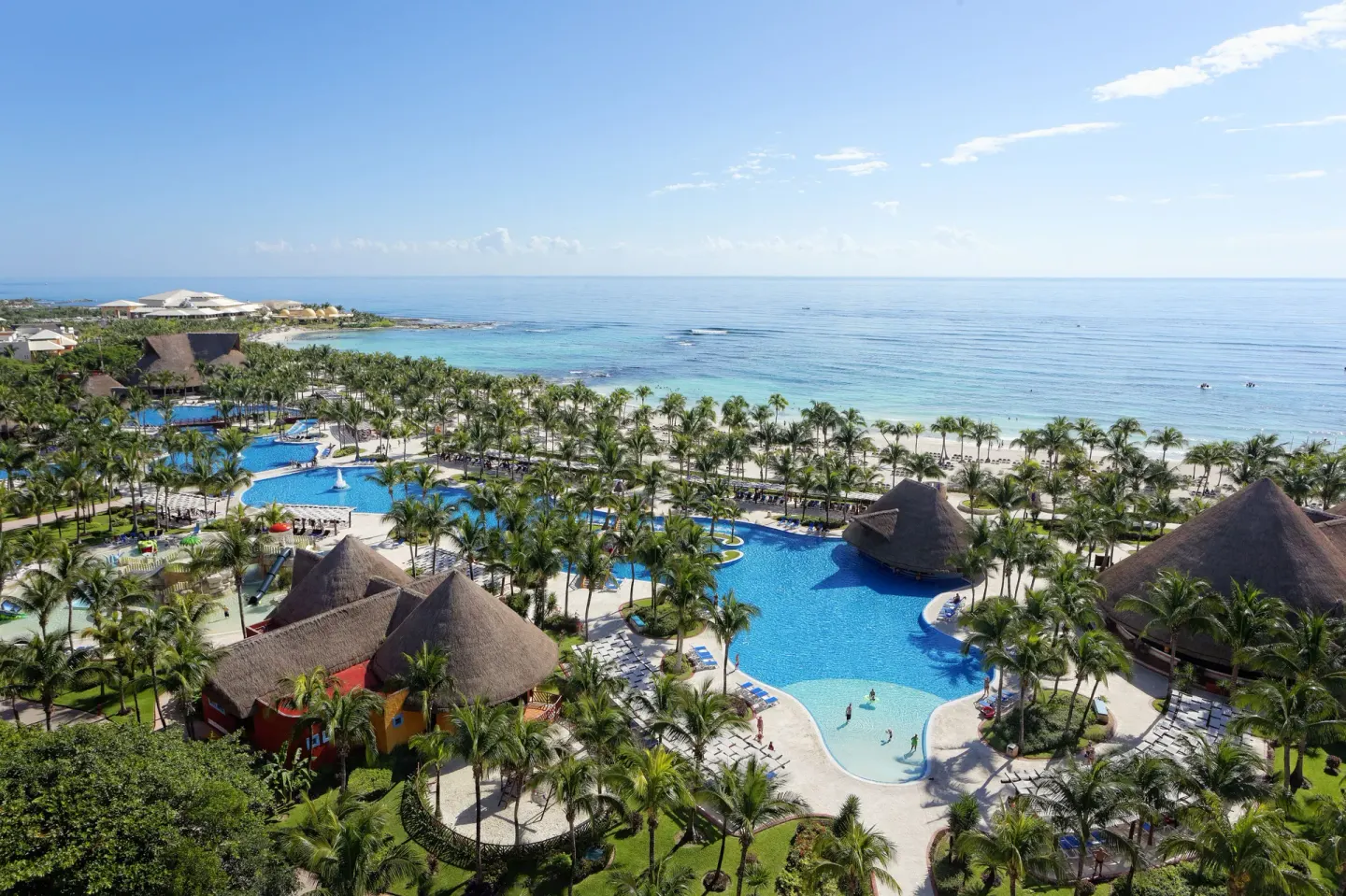 Aerial view of pools, palms, thatched roofs, and the sea at Barceló Maya Tropical.