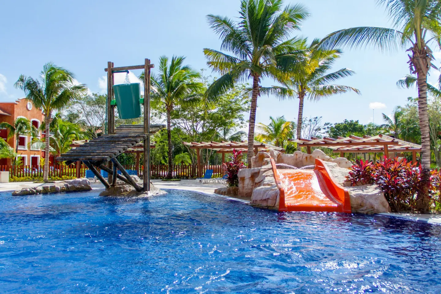 A children’s pool has a splash bucket and orange slide at Barceló Maya Tropical.
