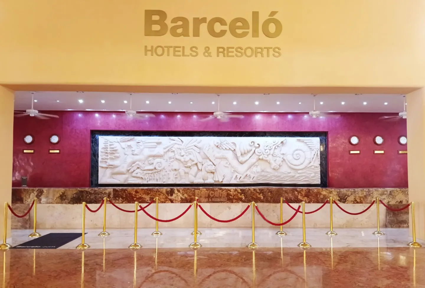 Reception desk with Barceló sign and red rope queue at Barceló Maya Tropical.