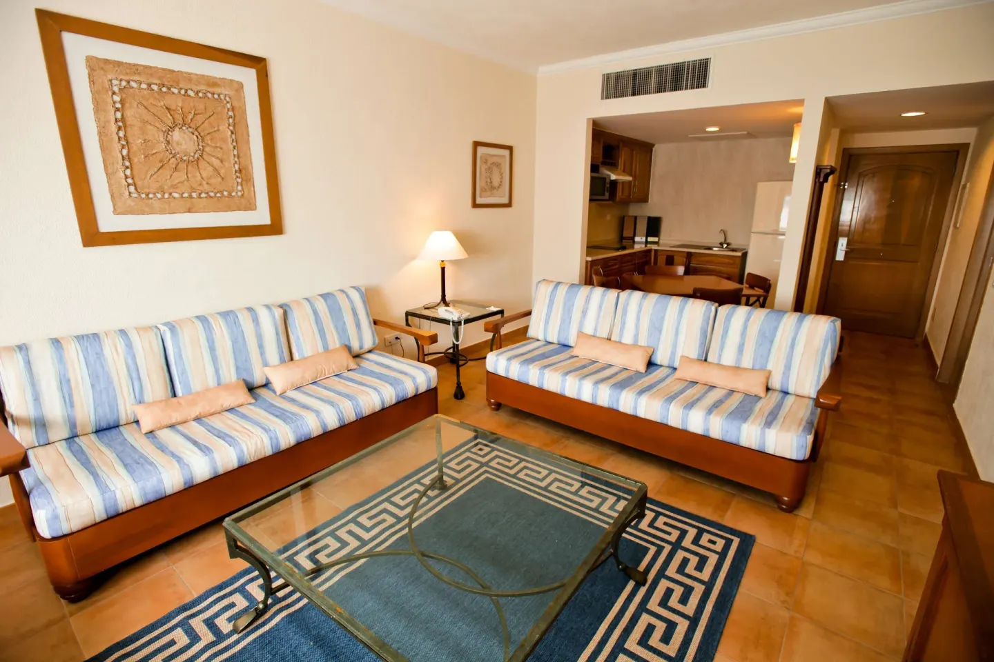 Living area with striped sofas, glass coffee table, and kitchenette at Barceló Maya Tropical.