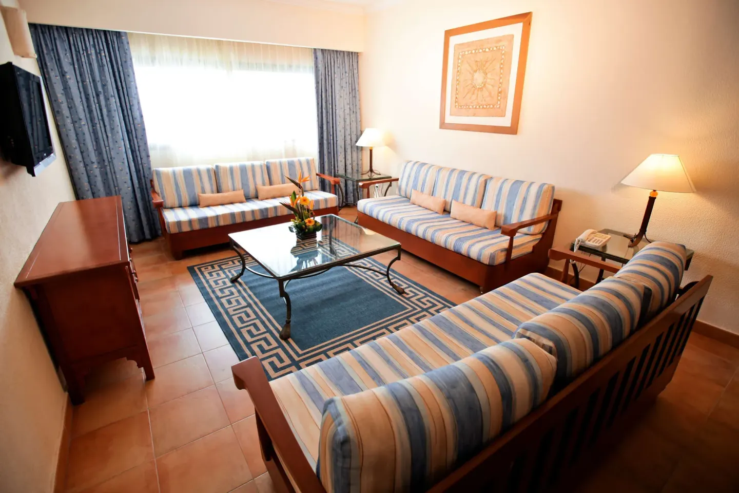 Guest room lounge with three striped sofas and blue rug at Barceló Maya Tropical.