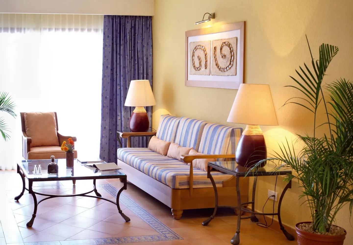 Suite sitting corner with striped sofa, armchair, lamps, and plant at Barceló Maya Tropical.