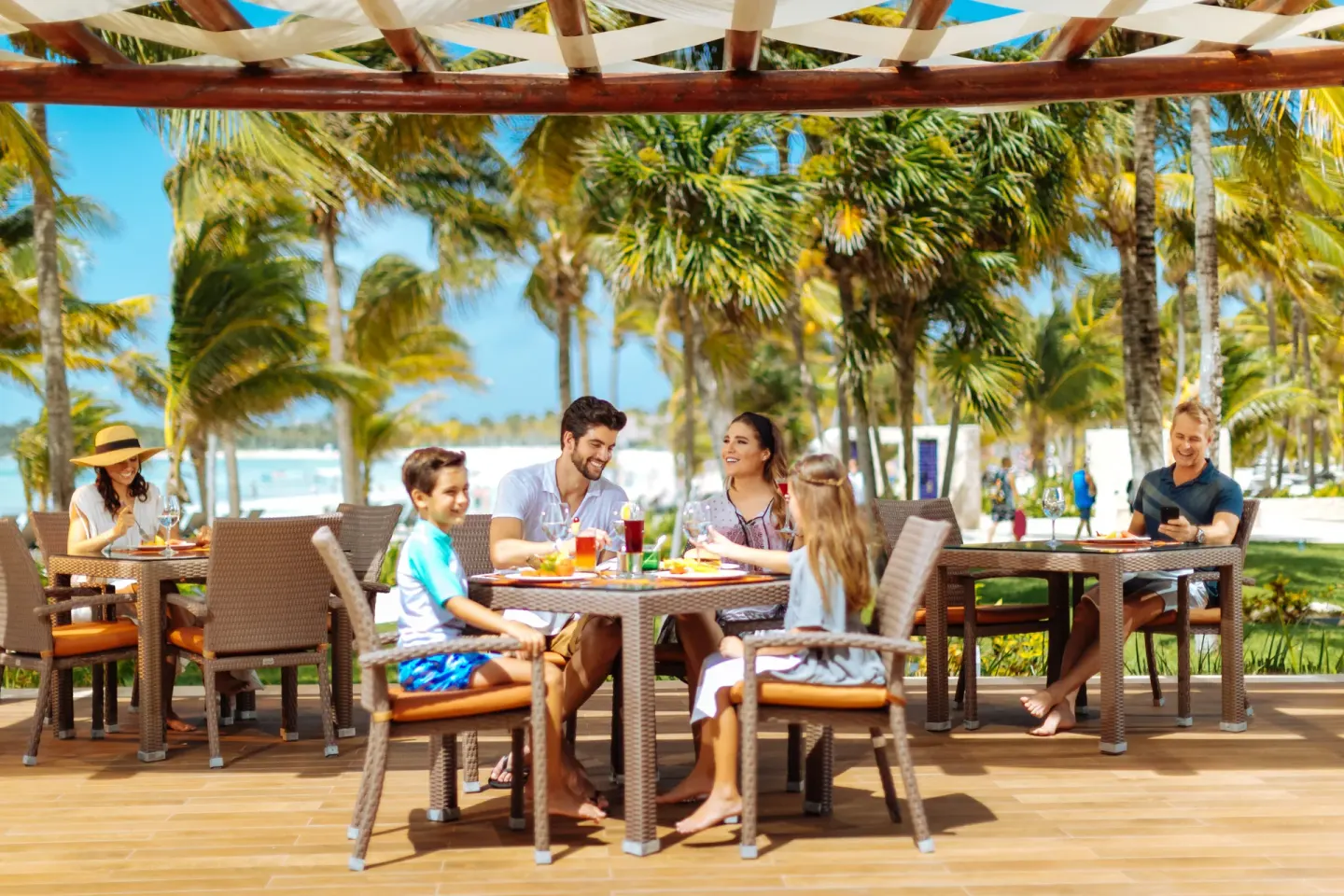 Outdoor terrace dining with palm trees and beach beyond at Barceló Maya Tropical.