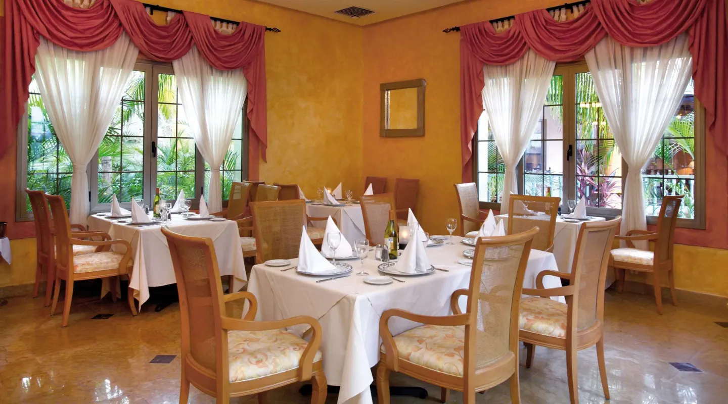 White-clothed restaurant tables by pink-draped windows at Barceló Maya Tropical.