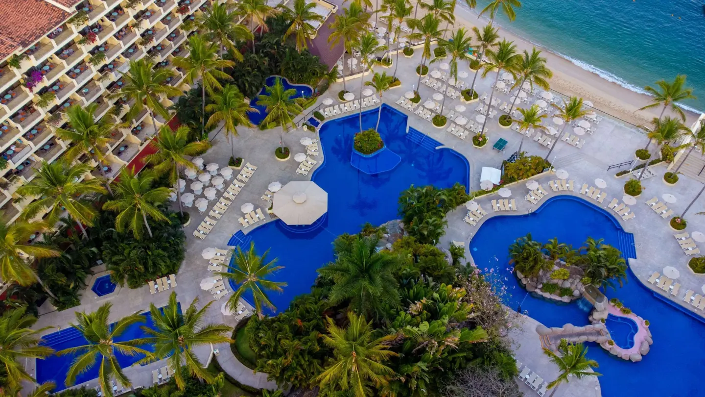 Aerial view of pools, palms, beach, and resort buildings at Barceló Puerto Vallarta.