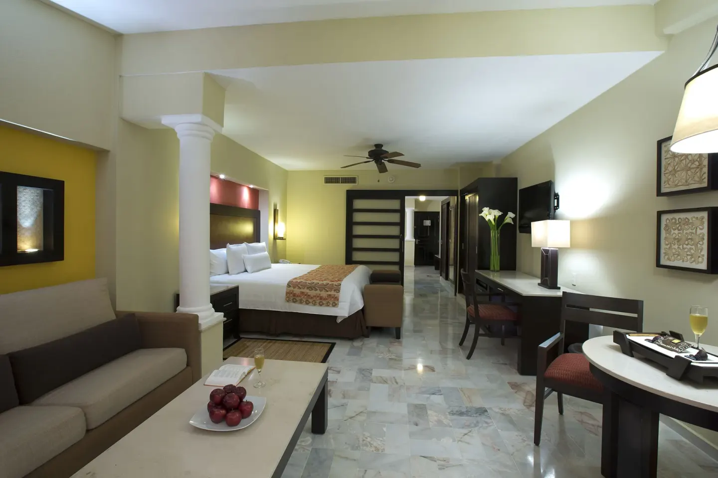 A guest room at Barceló Puerto Vallarta with a king bed, sofa, desk, and dining table.