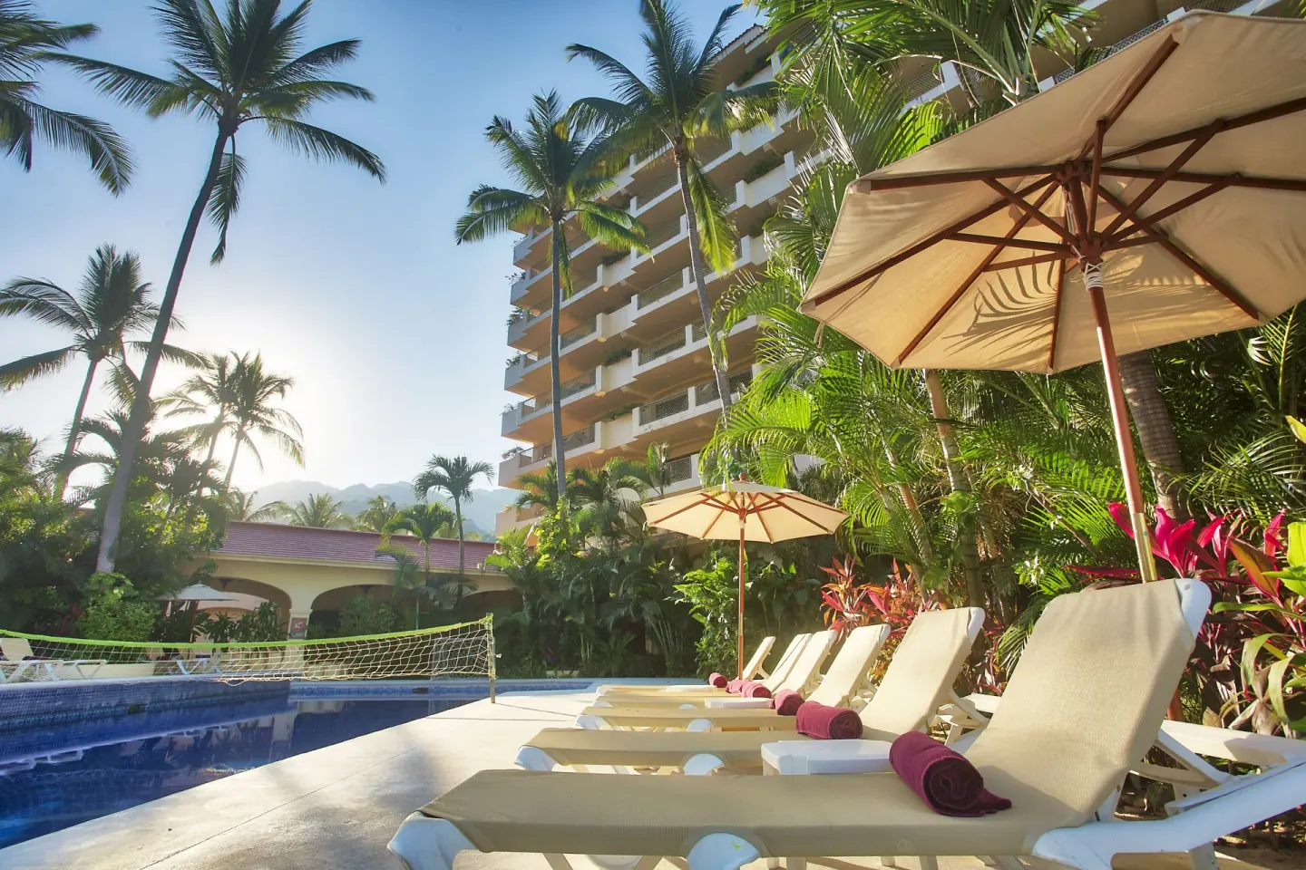 Poolside loungers under umbrellas beside palms at Barceló Puerto Vallarta.