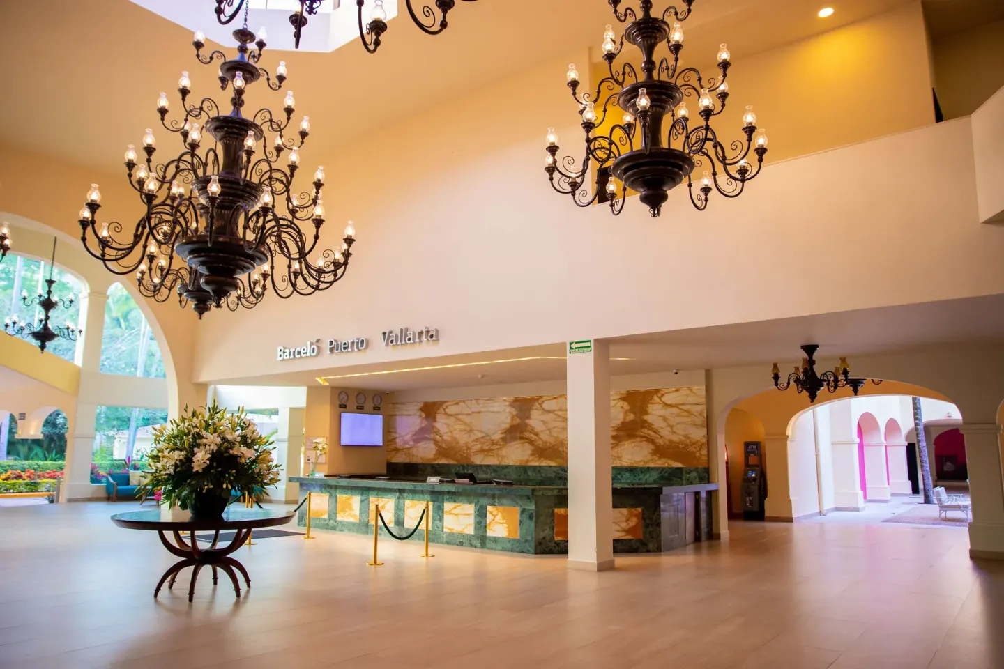 Reception desk at Barceló Puerto Vallarta beneath chandeliers with a flower arrangement nearby.
