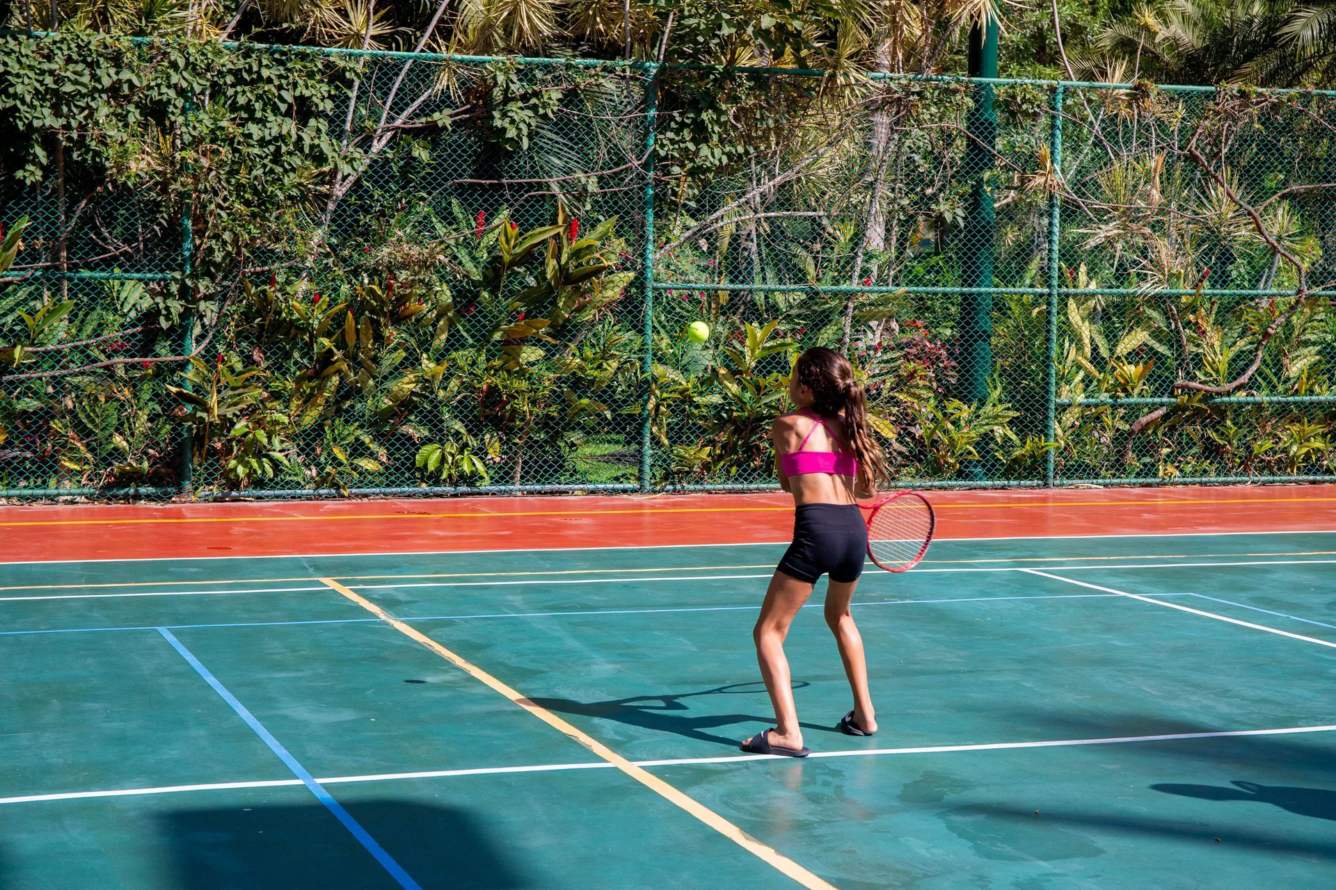 Child returning a tennis ball on an outdoor court at Barceló Puerto Vallarta.