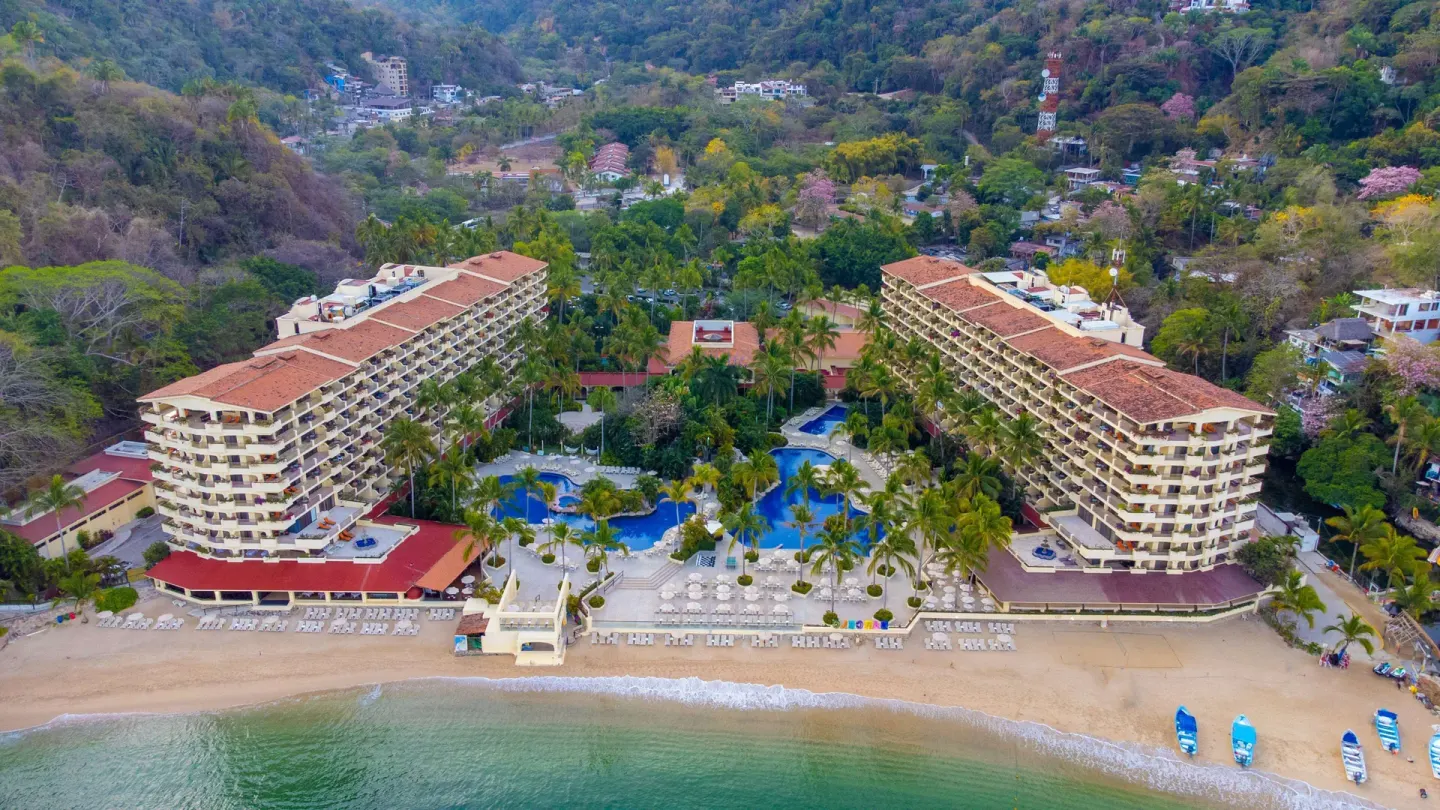 Wide aerial view of beachfront resort buildings and green hills at Barceló Puerto Vallarta.