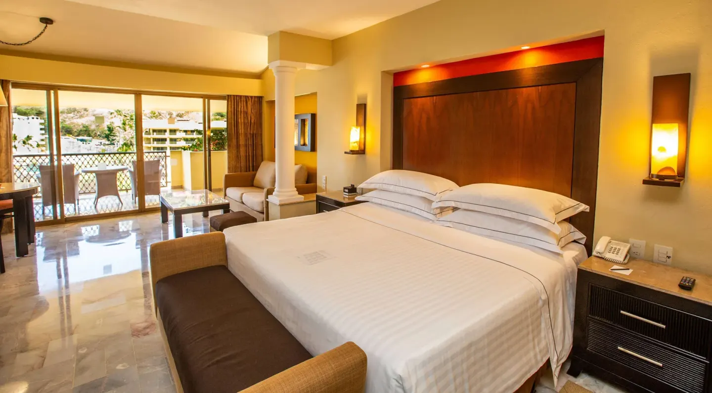Deluxe Suite Premium Level king bed and balcony doors at Barceló Puerto Vallarta.