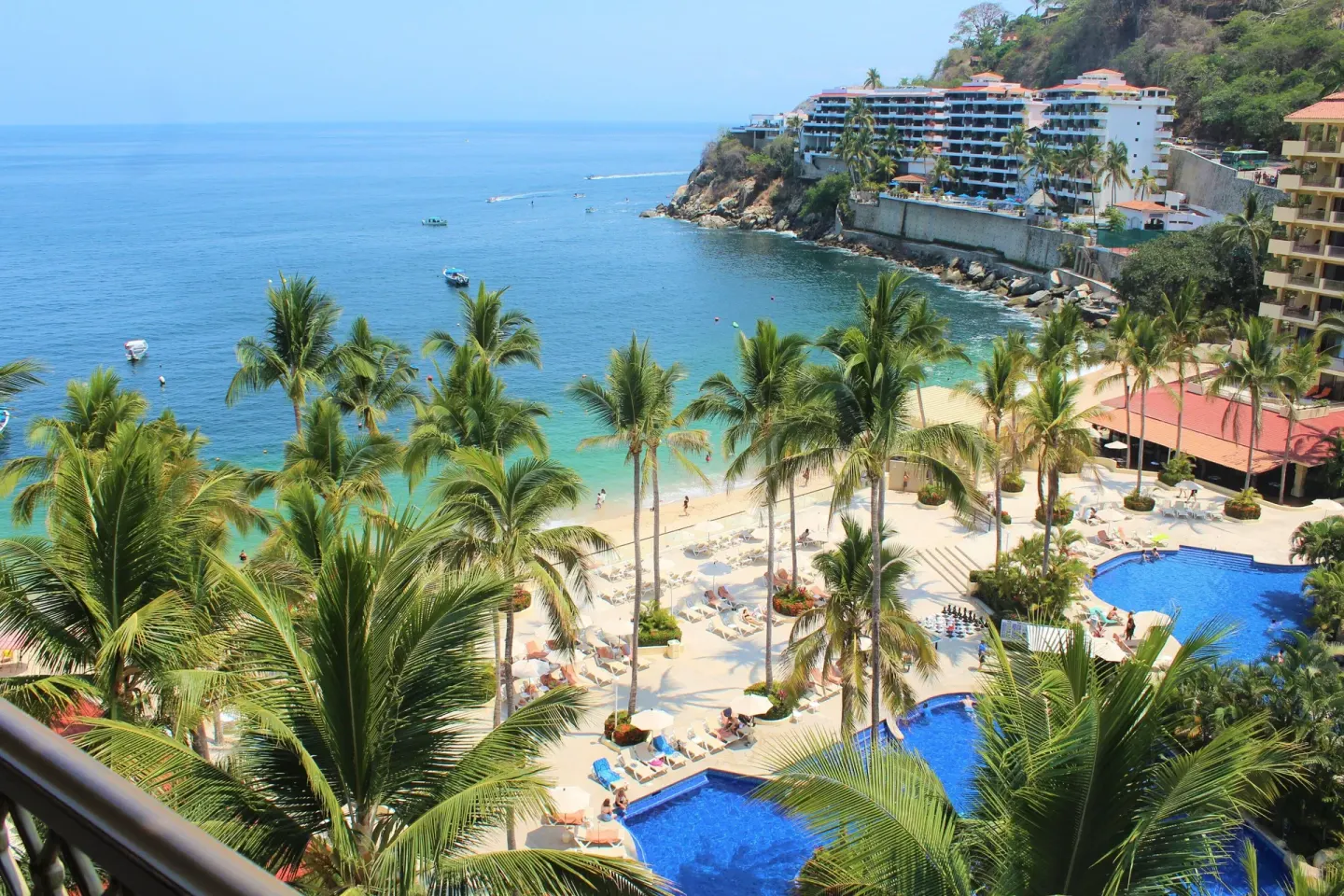Deluxe Suite balcony view of pools, palms, beach and bay at Barceló Puerto Vallarta.