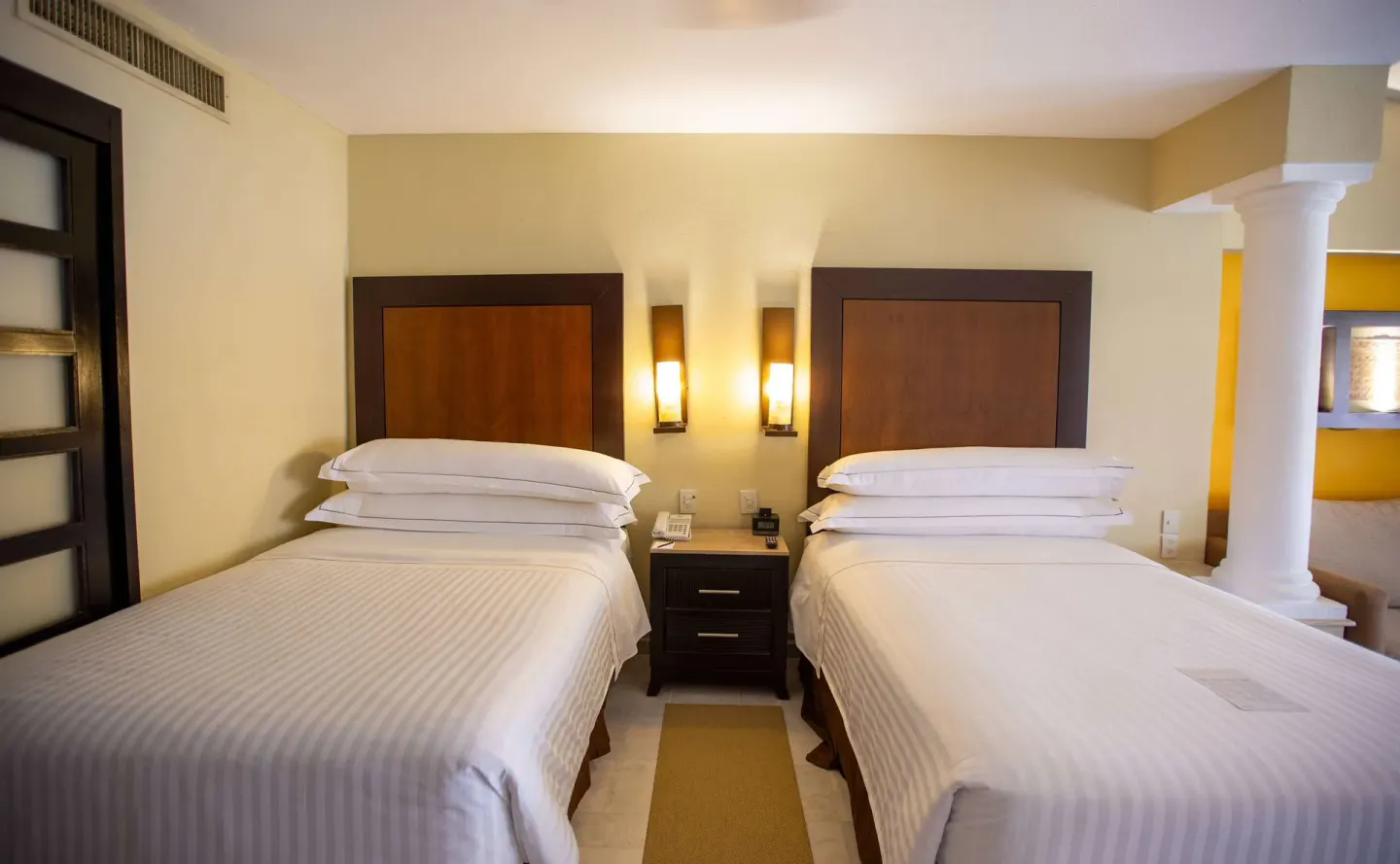 Deluxe Suite two beds with bedside table and wall lamps at Barceló Puerto Vallarta.