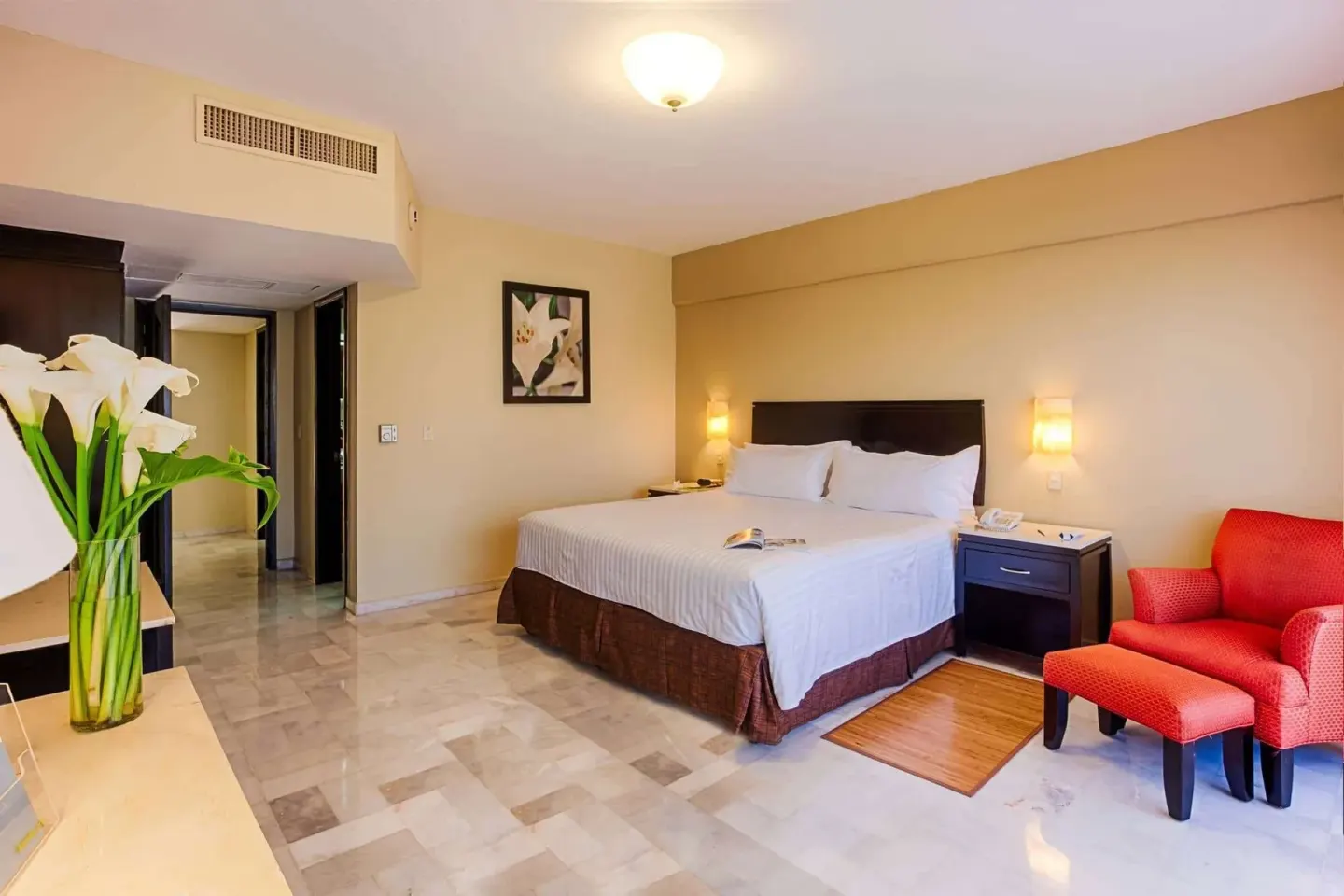 Family Room king bed with red armchair and lilies at Barceló Puerto Vallarta.