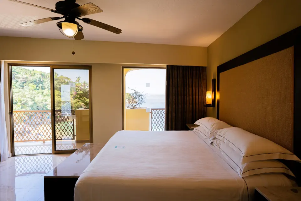 Master Suite king bed beside balcony doors with partial ocean view at Barceló Puerto Vallarta.