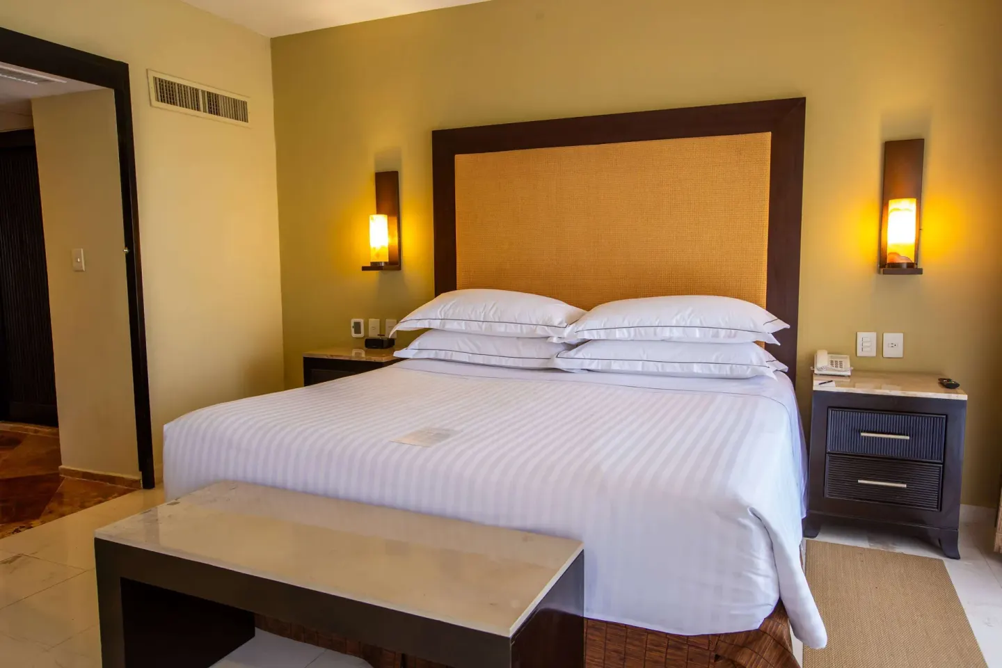 Master Suite bedroom with king bed, wall sconces and bench at Barceló Puerto Vallarta.