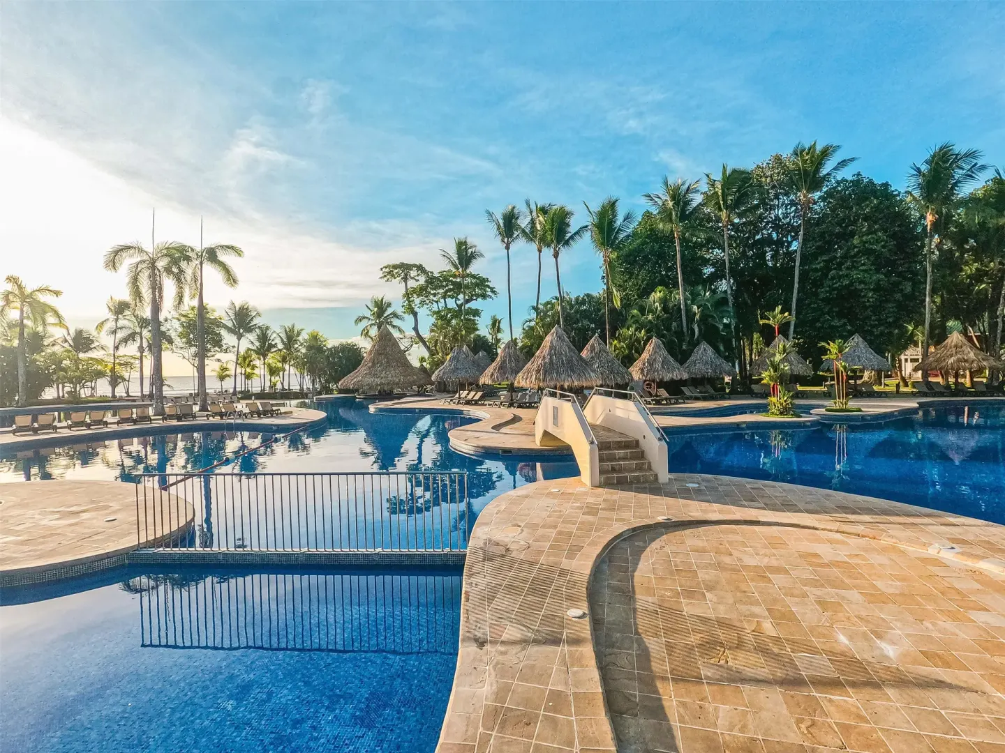 Wide resort pool with footbridge, palapas, and palm trees at Barceló Tambor.