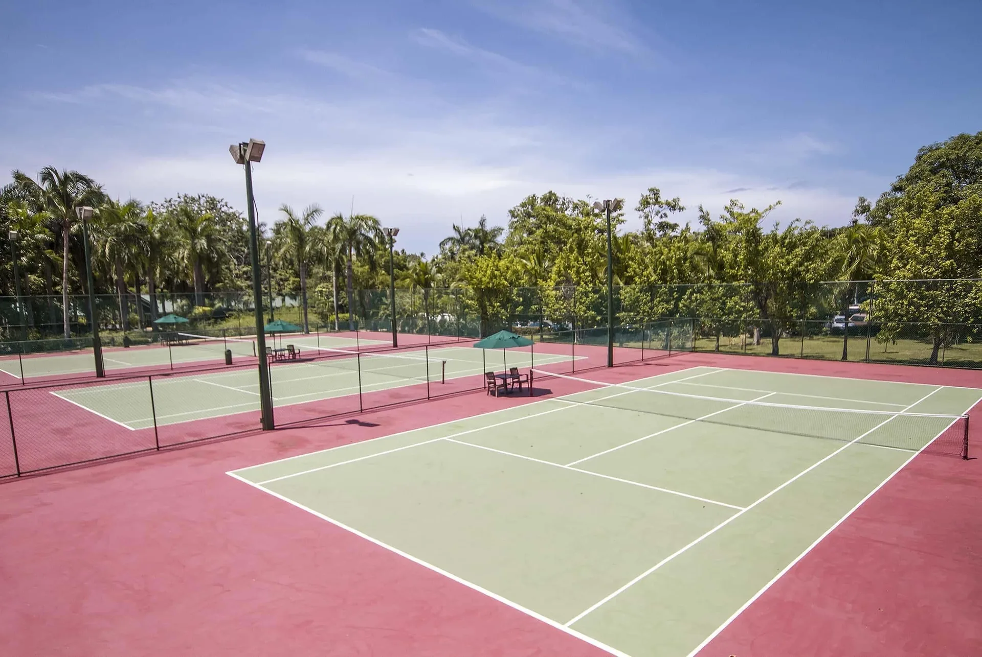 Tennis courts with red surrounds, nets, lights, and trees at Barceló Tambor.
