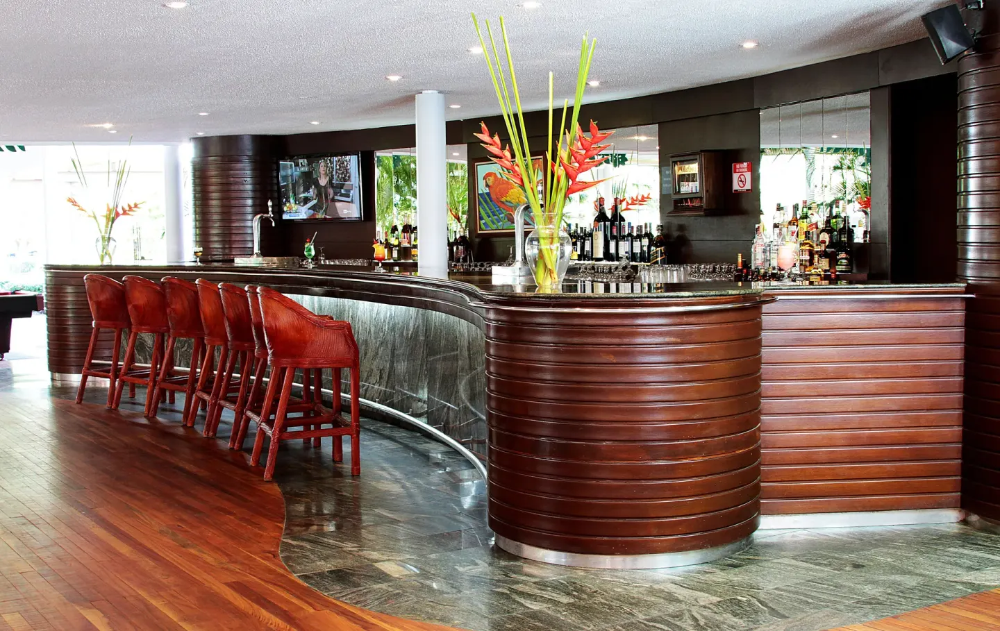 Curved wood bar with red stools and tropical flowers at Barceló Tambor.