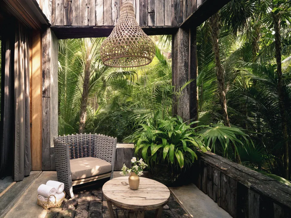 Small balcony with wicker chair and round table among palms at BE Destination Tulum