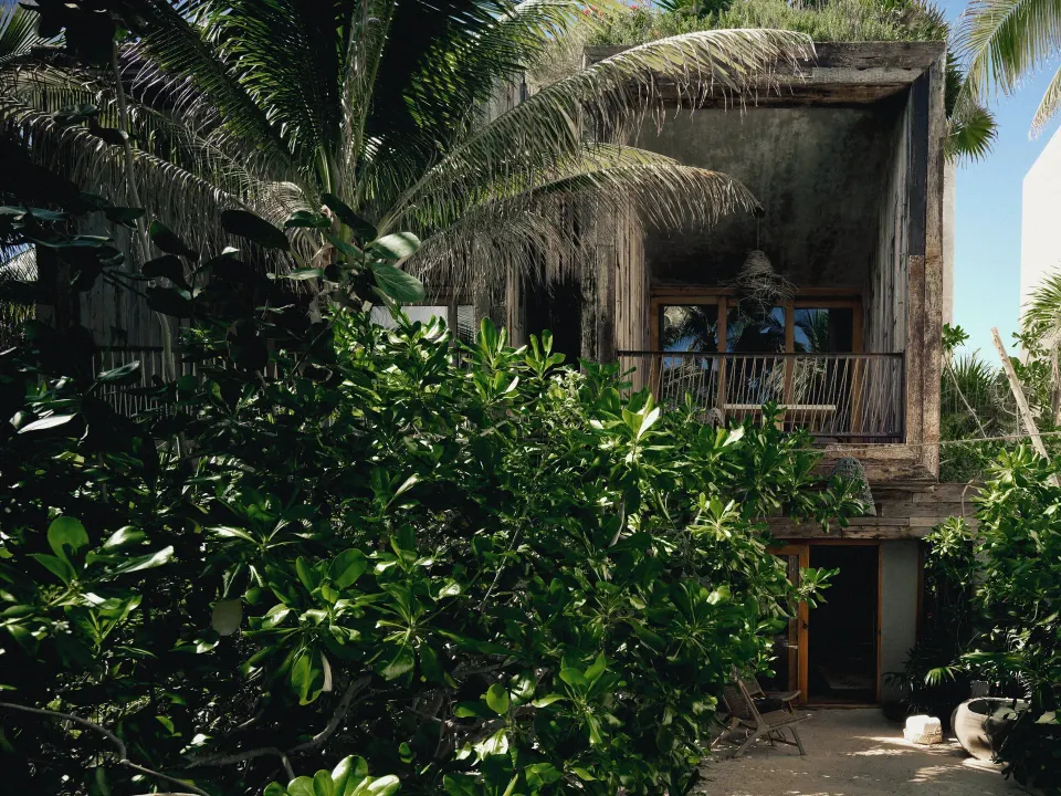 Resort building facade and balcony peeking through dense tropical foliage at BE Destination Tulum