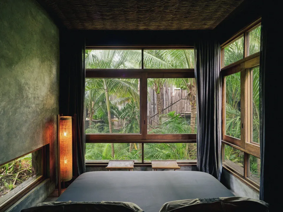 King bed with large windows overlooking tropical palms at BE Destination Tulum