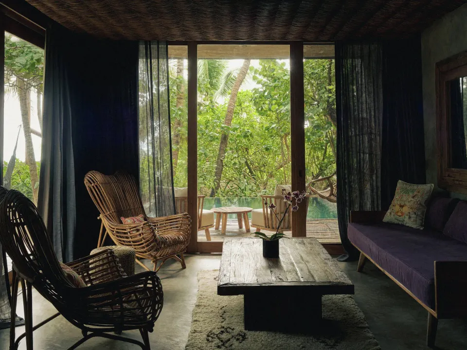 Cozy living area with rattan chairs and sliding glass doors opening to jungle at BE Destination Tulum