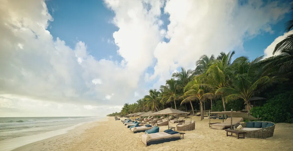 Wide beach panorama with rows of daybeds and palm trees under a dramatic sky at BE Destination Tulum