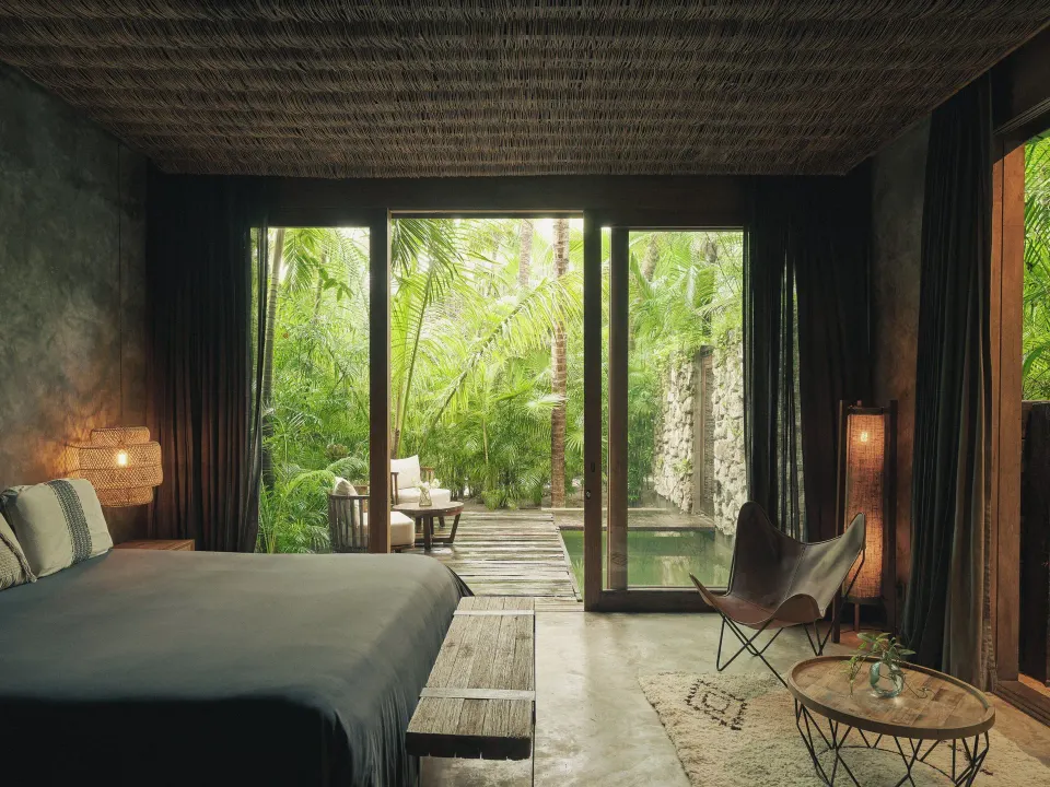 Guest room with large glass doors opening to a private plunge pool surrounded by palms at BE Destination Tulum