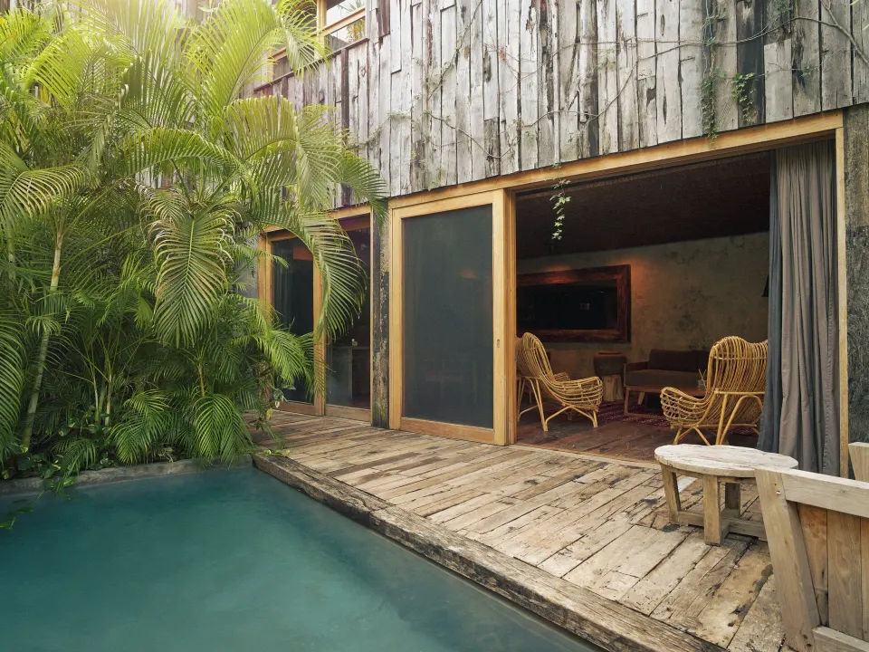 Private plunge pool and wooden deck opening to a suite with wicker chairs at BE Destination Tulum
