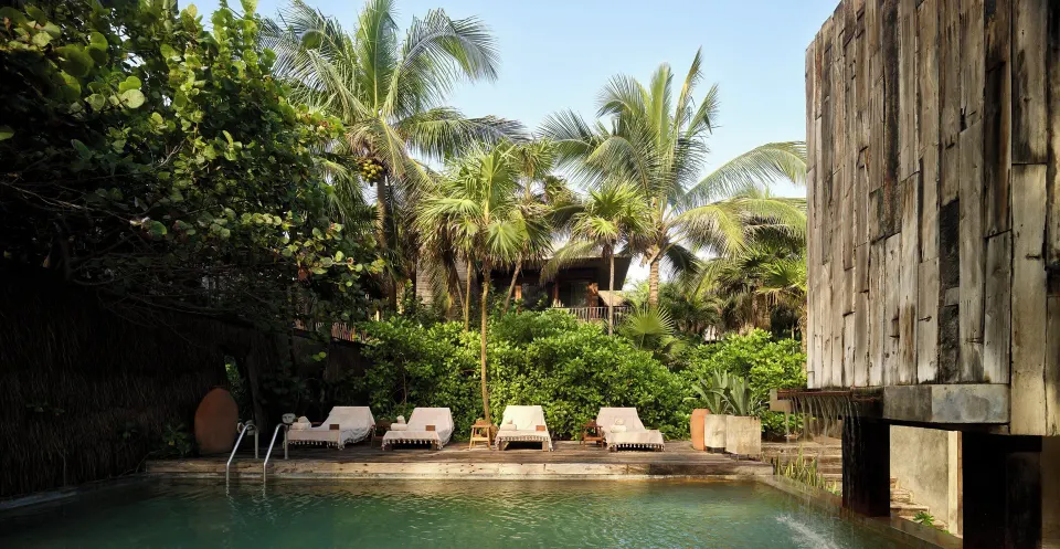 Poolside loungers beneath palms in a private resort pool area at BE Destination Tulum
