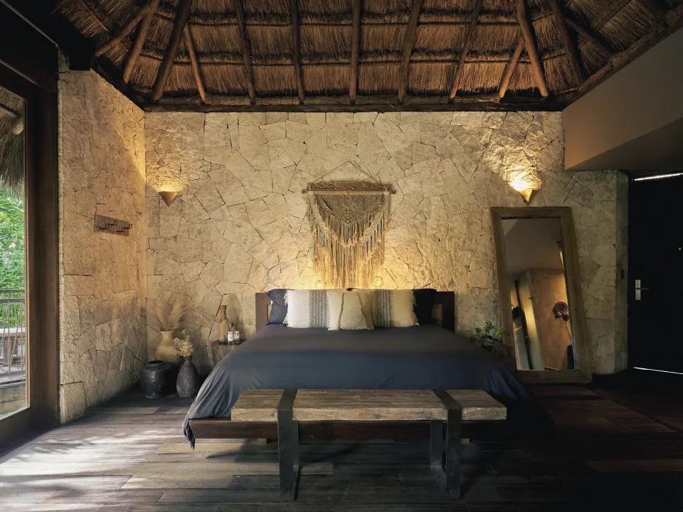 Bedroom with king bed, textured stone wall and macramé decoration at BE Destination Tulum