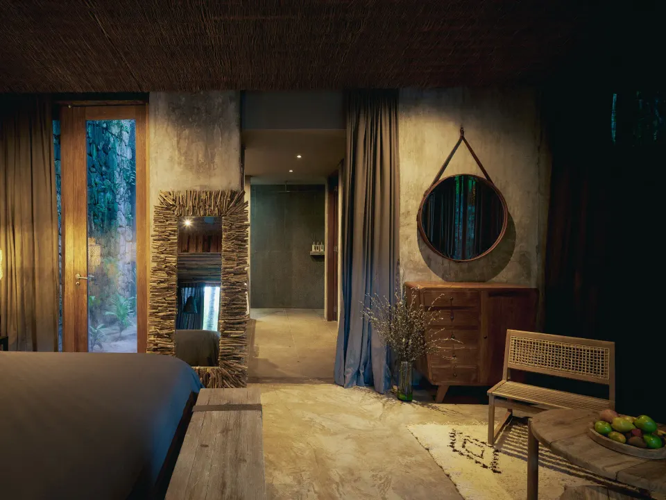 Guest bedroom view toward doorway with round mirror and bench at BE Destination Tulum