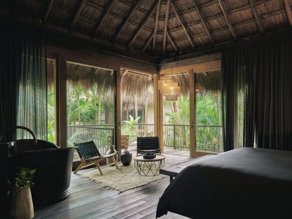 Thatched-roof guest room with king bed and balcony overlooking tropical foliage at BE Destination Tulum