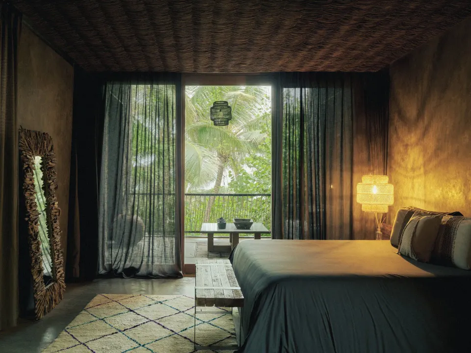 Dark, tropical guest room with king bed and balcony framed by palms at BE Destination Tulum