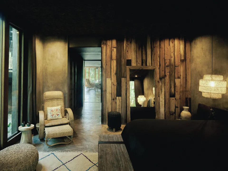 Dimly lit bedroom with dark linens and reclaimed wood wall at BE Destination Tulum