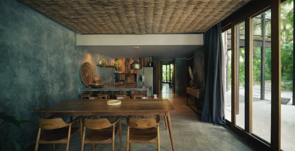 Indoor dining table and open kitchen with sliding doors to an outdoor terrace at BE Destination Tulum