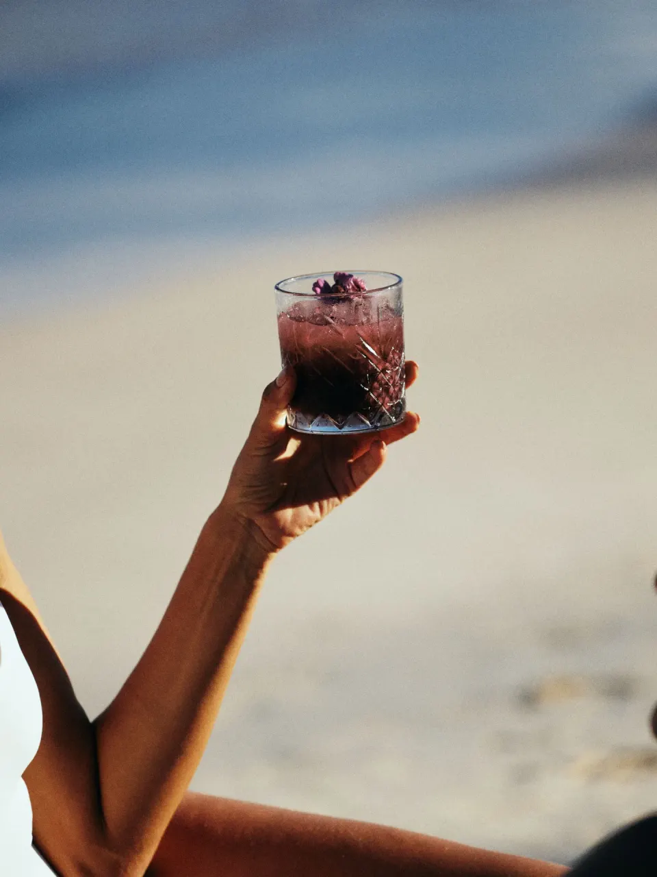 Hand holding a purple cocktail beside the beach at BE Destination Tulum