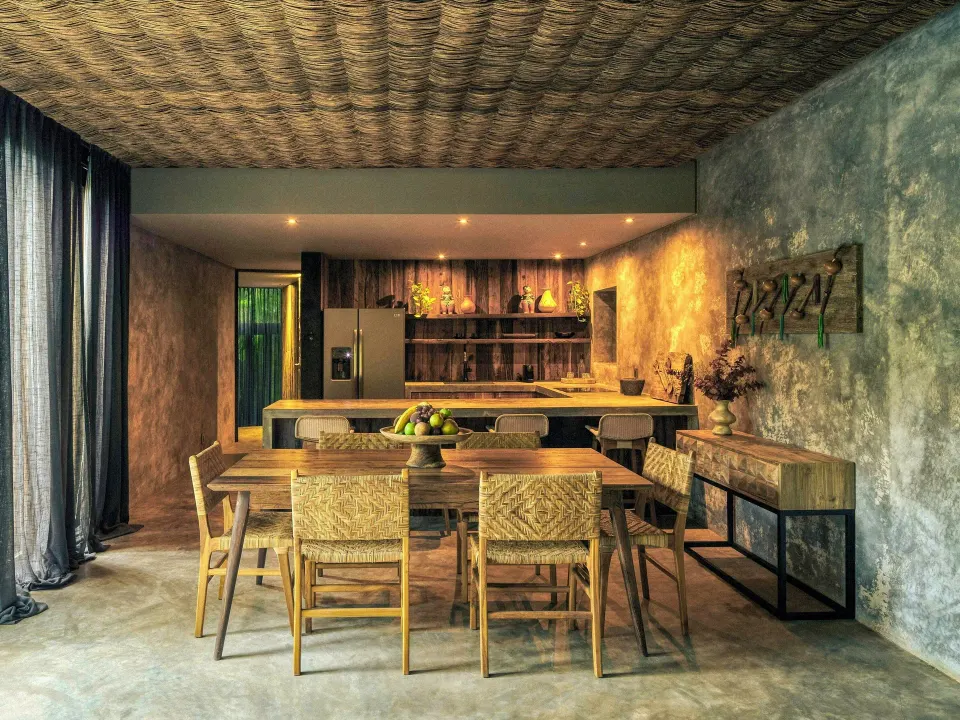 Dining table and open kitchen with woven ceiling in a Premier Palm Suite at BE Destination Tulum