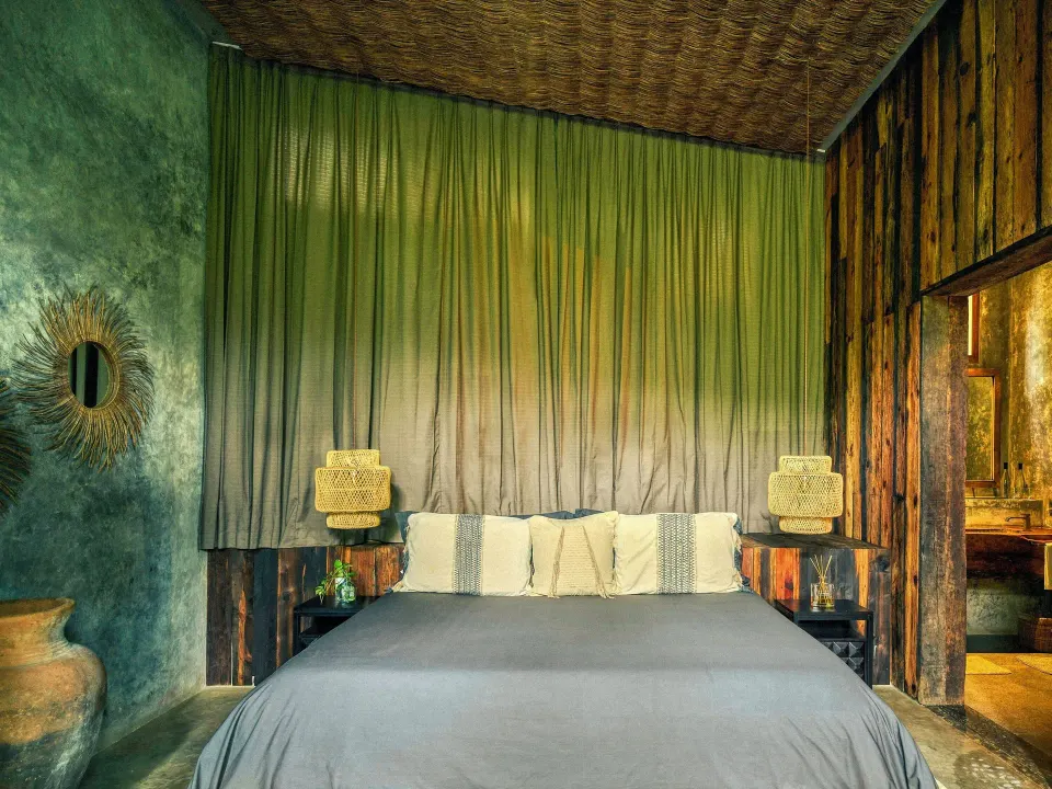 King bed with textured wood headboard and draped curtains in a Premier Palm Suite at BE Destination Tulum
