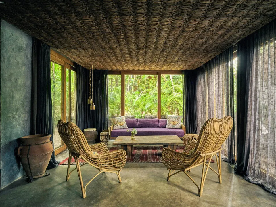 Living area with rattan chairs and sofa overlooking lush greenery in a Premier Palm Suite at BE Destination Tulum